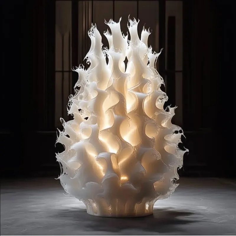 A tall white sculptural candle with a wave-crest surface, glowing from inside