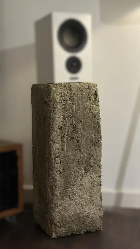 A tall raw concrete plinth with a speaker on top, in a living room